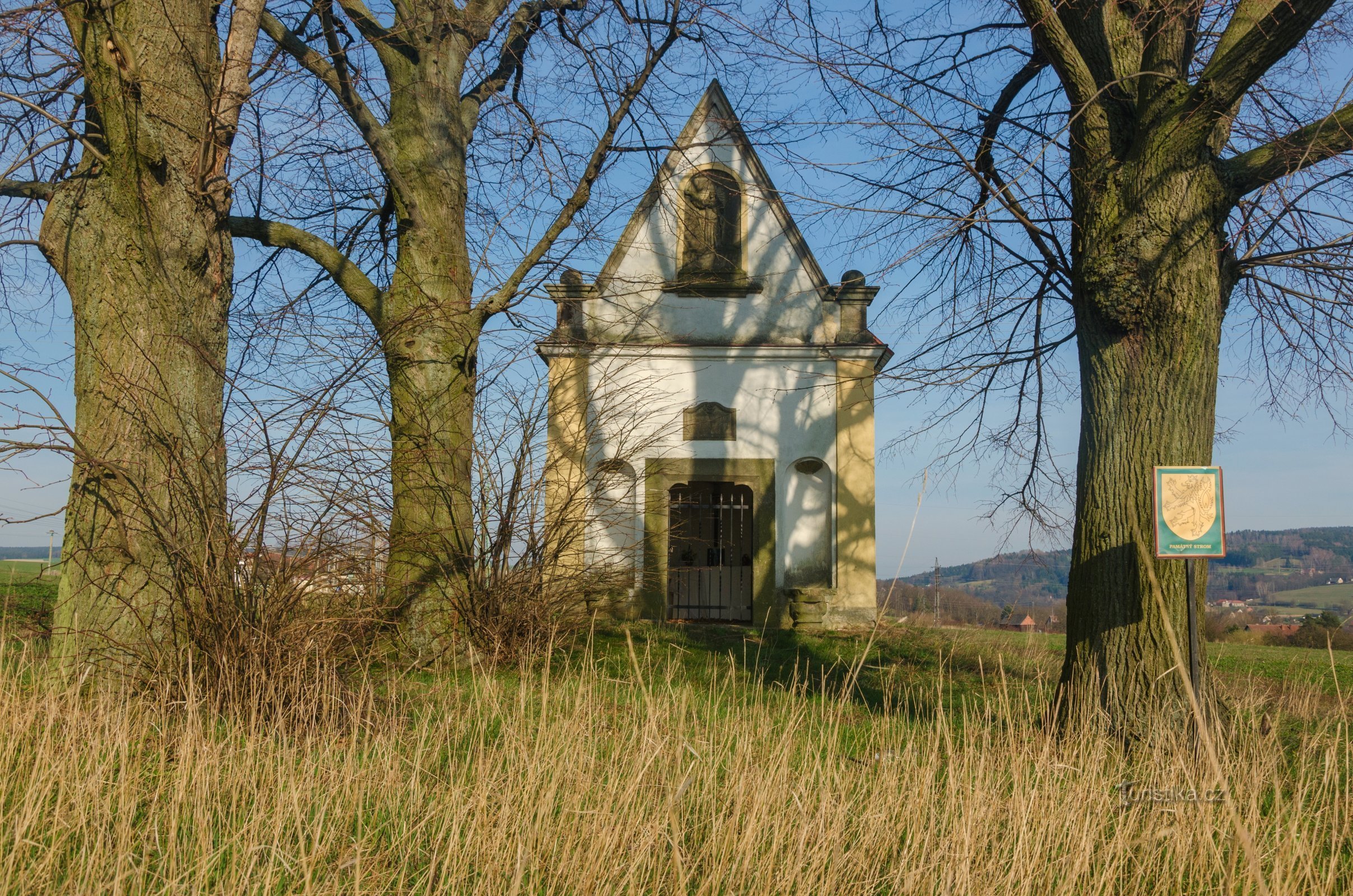 De barokke kapel van Allerheiligen achter de vrijheidslindebomen, op de achtergrond een deel van de Litický hřebet