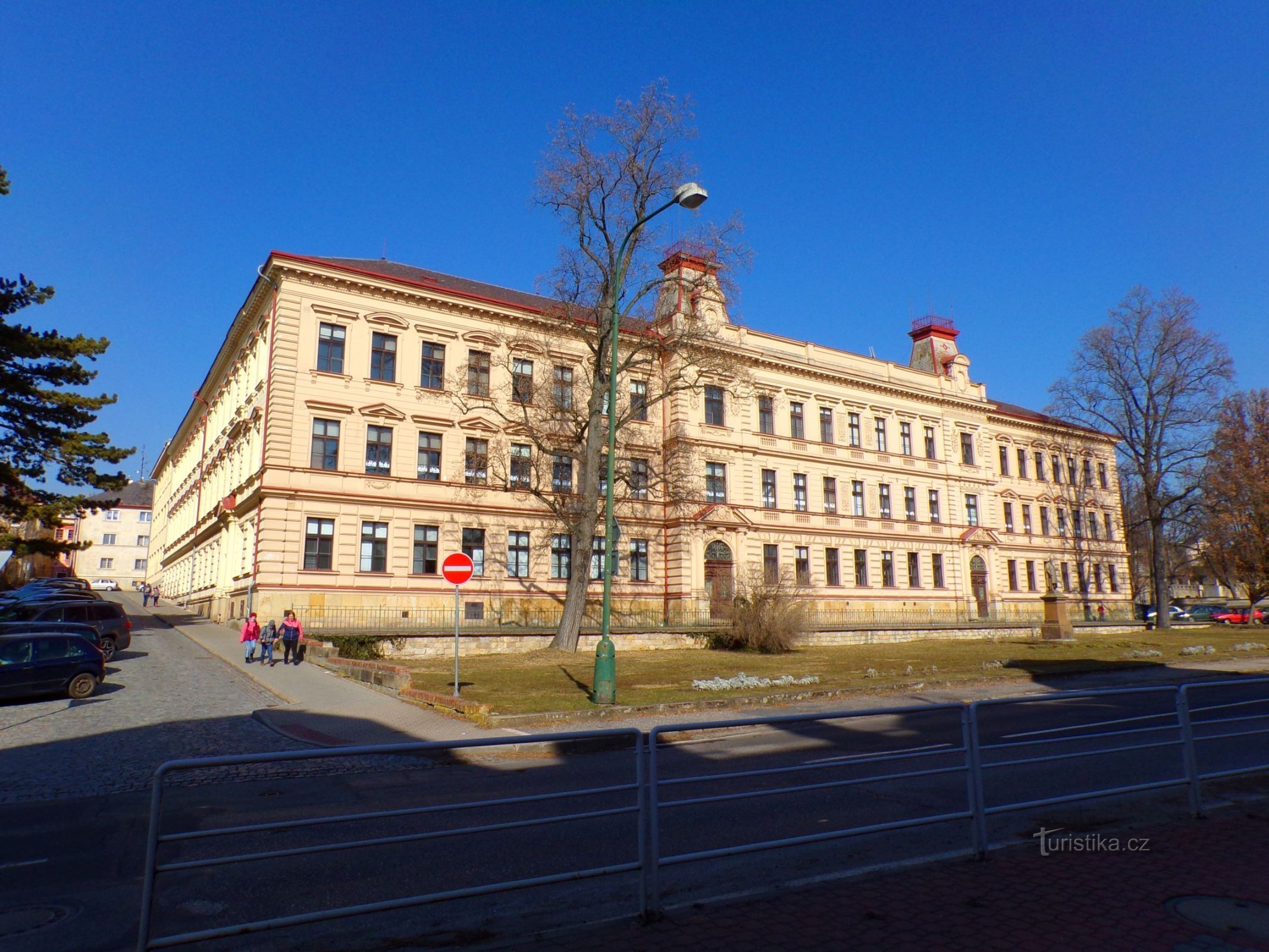 El edificio de la primera escuela primaria con el monumento a Jan Amos Comenius en primer plano (Jičín, 1/3.3.2022/XNUMX)