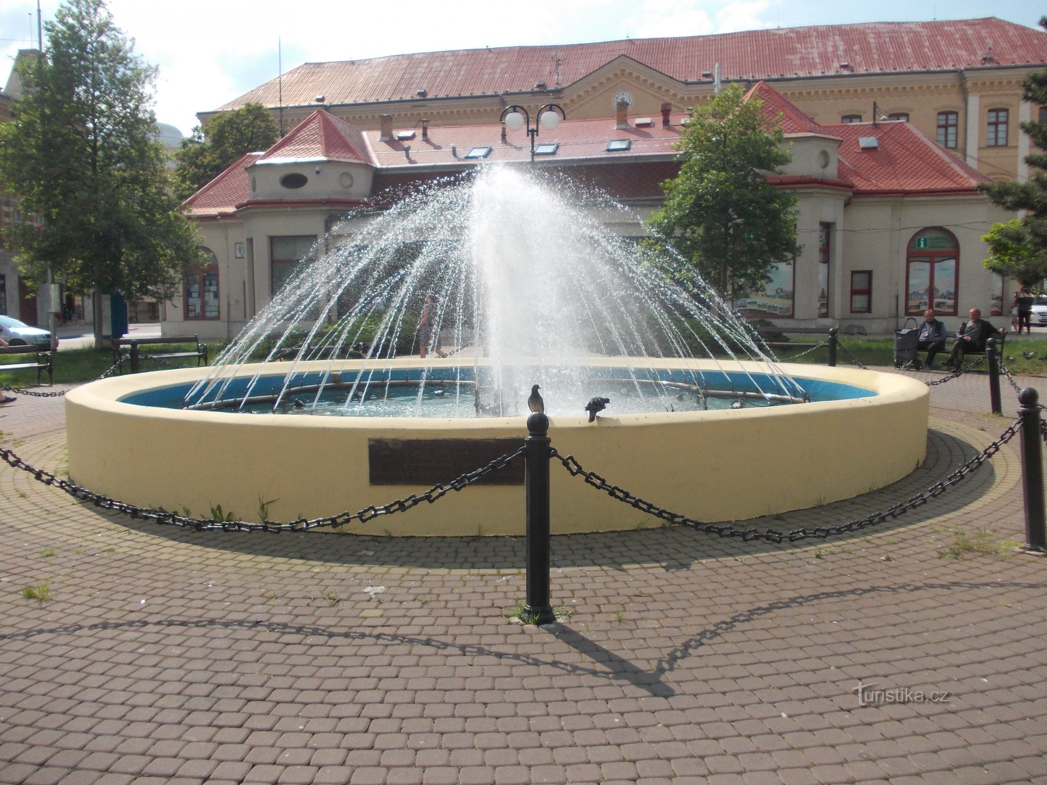 la fontaine et le bâtiment de l'école tout au fond