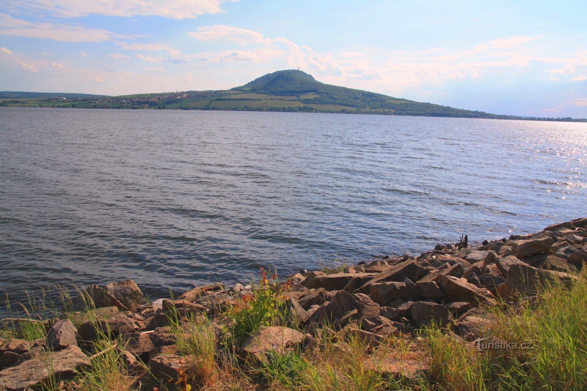 Op de dijk opent zich een zicht op het uitgestrekte oppervlak van het Novomlýnská-stuwmeer met de top van de Pálava