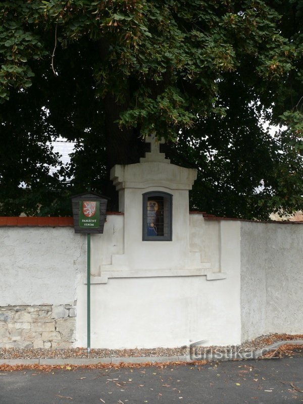Borne et chapelle dans le mur près du tronc de tilleul