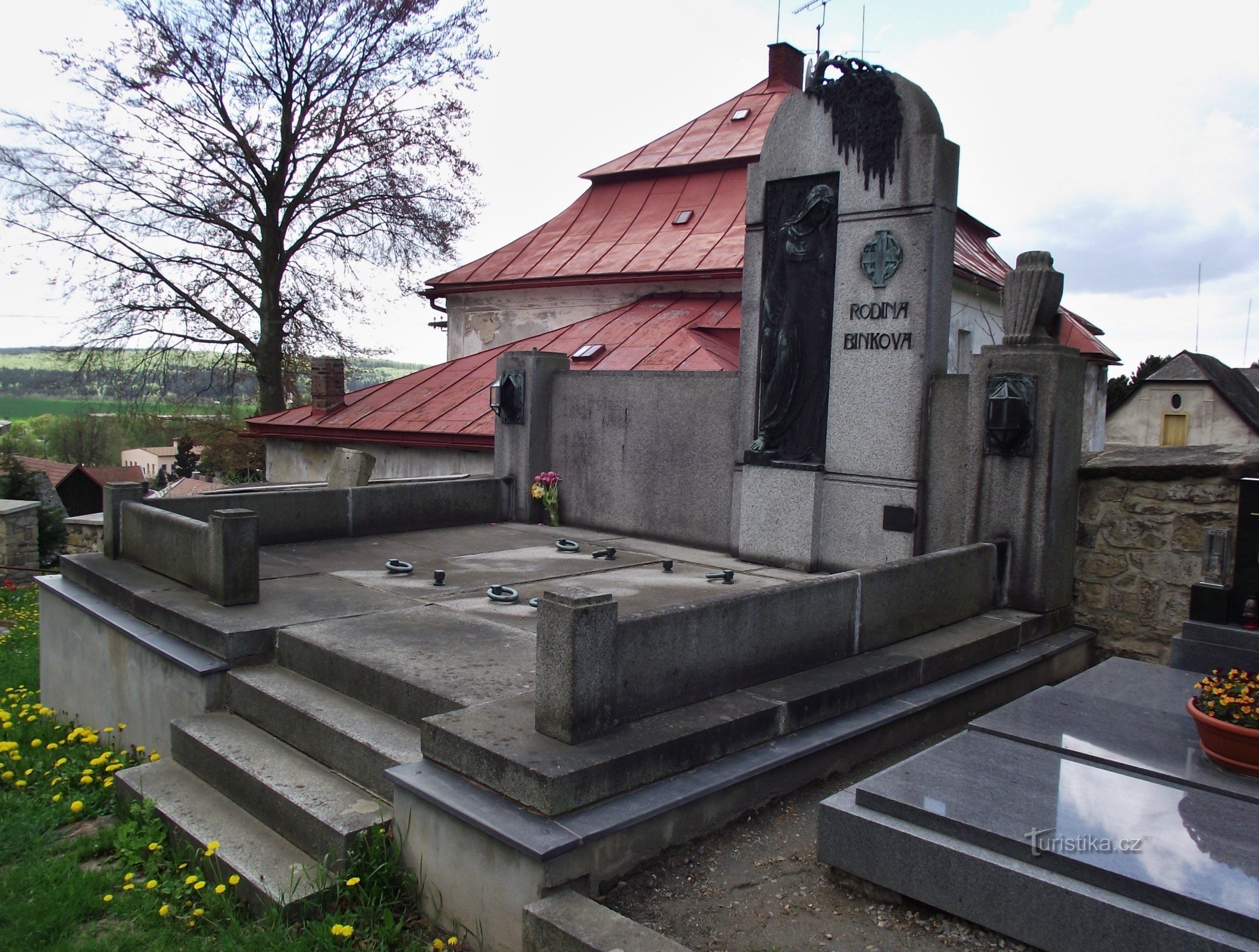 eine Skulptur der Bildhauerin Jana Štursa auf dem Grab der Familie Bink, im Hintergrund des Pfarrhauses