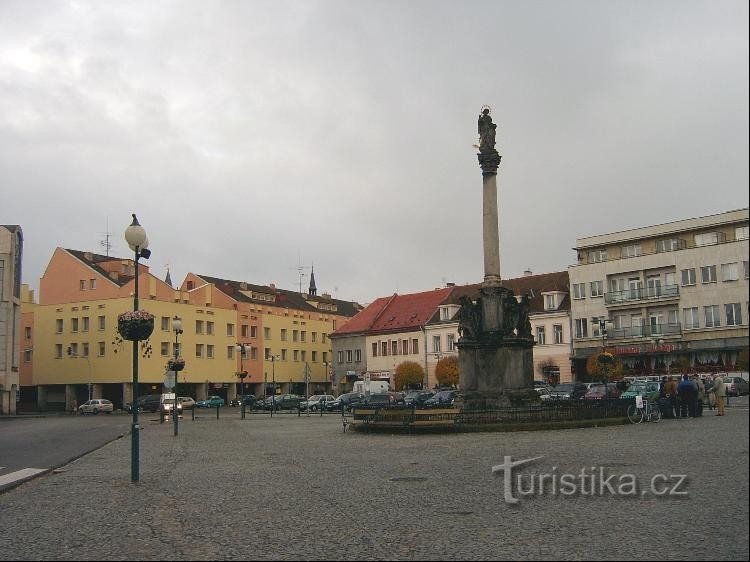 vedere de la est: coloana ciumei, pe fundal fațada galbenă a centrului comercial Eliška