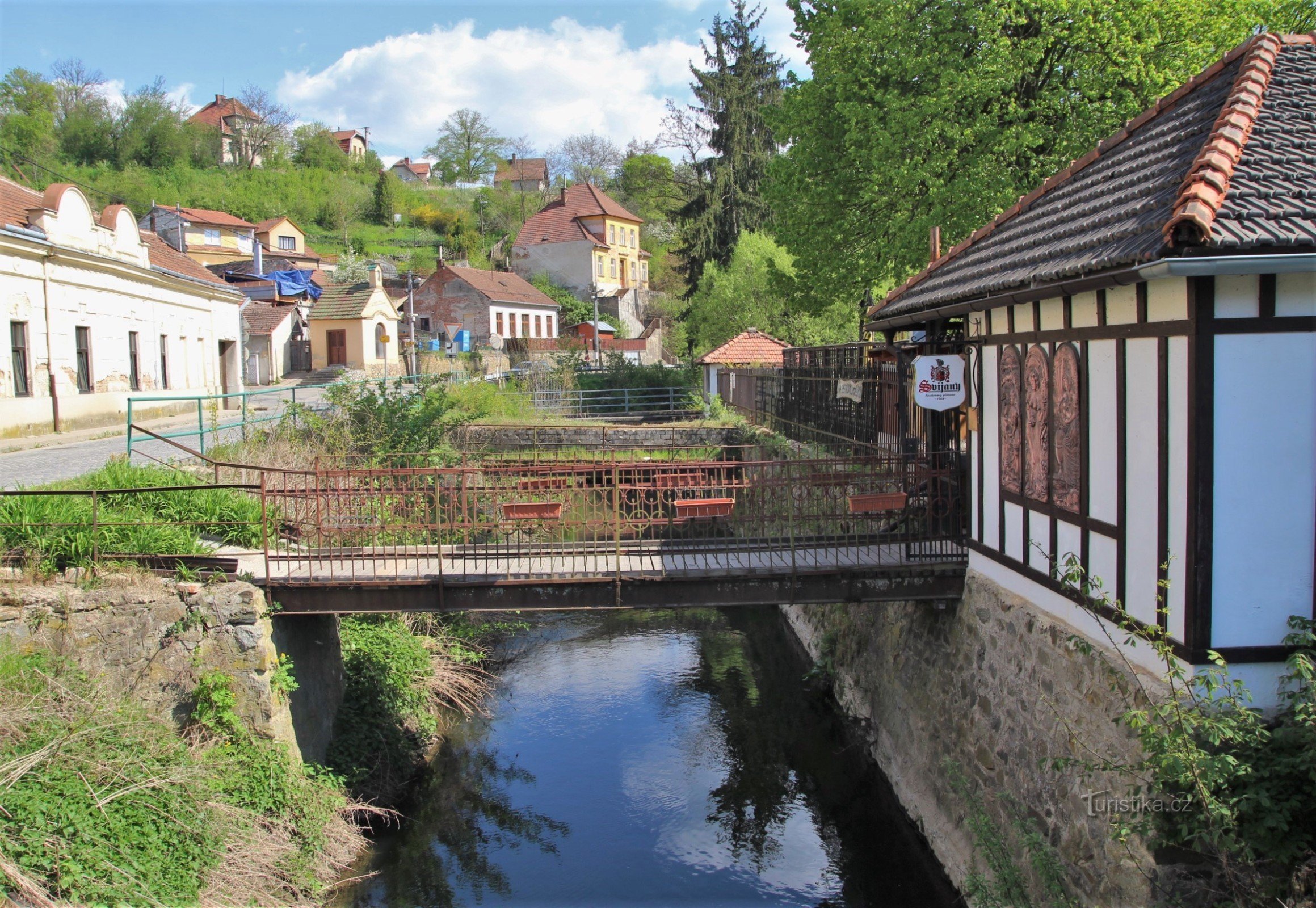 Uma vista da estrada, em primeiro plano a ponte que leva ao pub, atrás dela o rio Ča