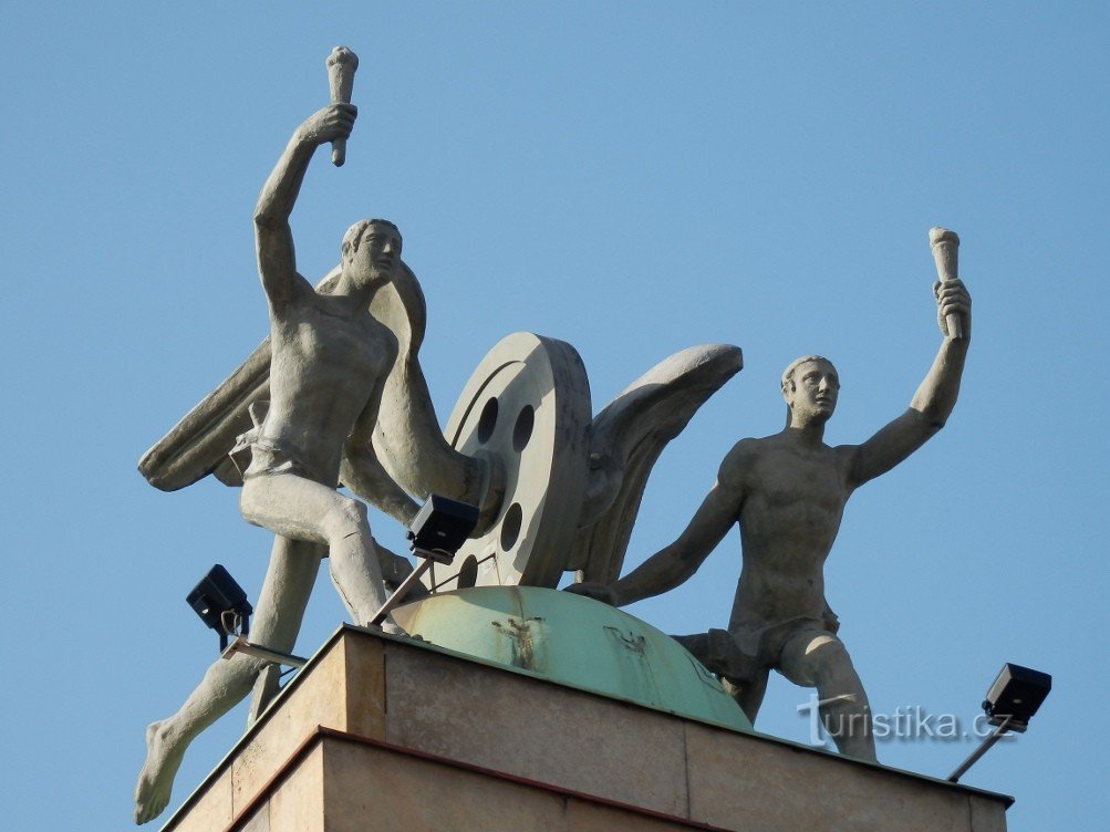 Een sculptuur van lampdragers en een gevleugeld wiel